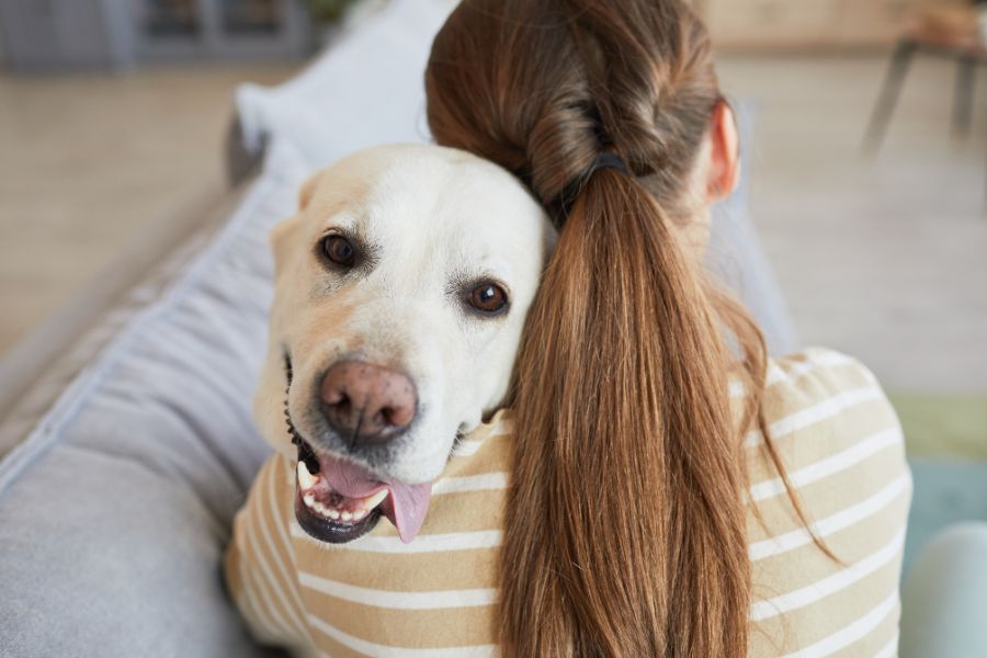 ragazza sul divano abbraccia il suo cane che sorride all'obiettivo