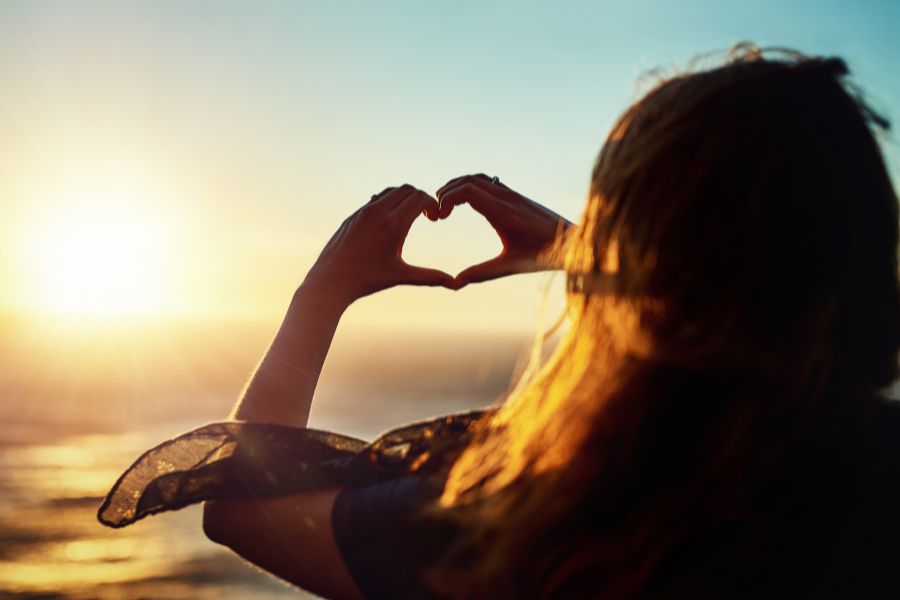 ragazza di spalle fa il simbolod el cuore con le mani al tramonto sulla spiaggia