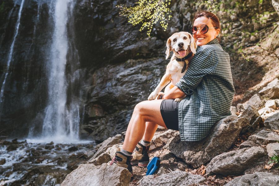 una ragazza abbraccia il suo cane davanti a una cascata in montagna